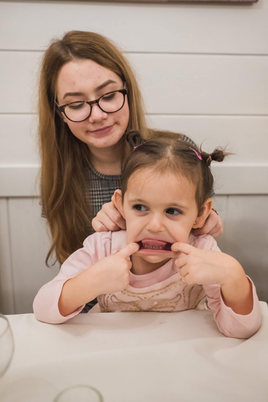 škeriace sa dievčatko ktoré sedí na kolenách mladej ženy