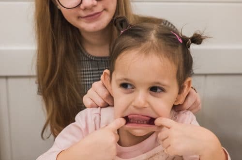 škeriace sa dievčatko ktoré sedí na kolenách mladej ženy